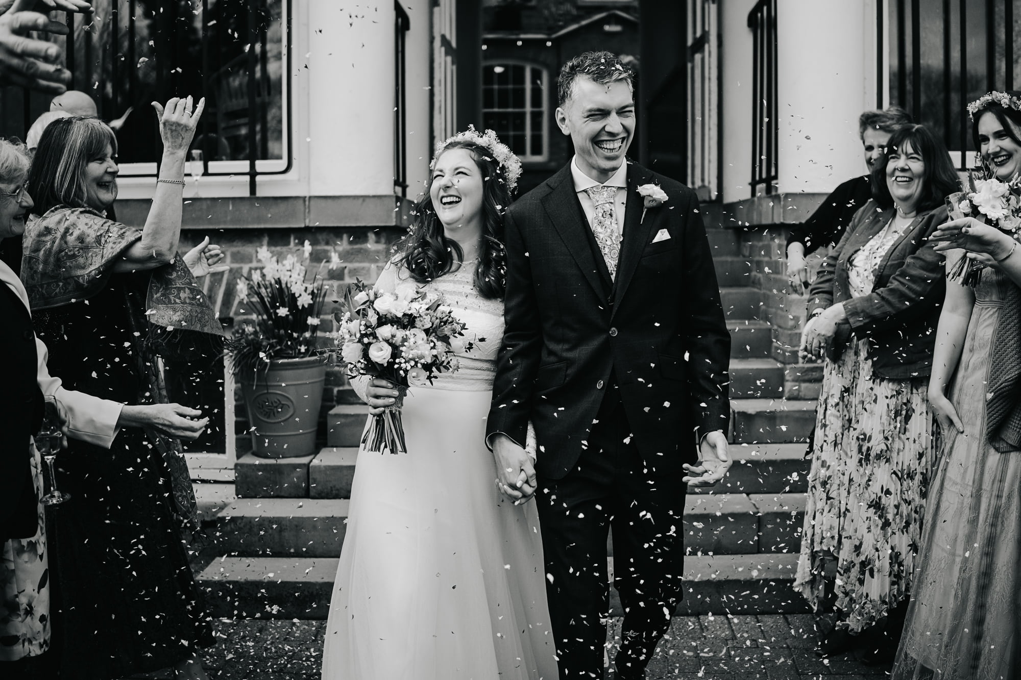 Couple walking through confetti, thrown by their guests at a wedding at St Chad's College Durham Wedding in black and white